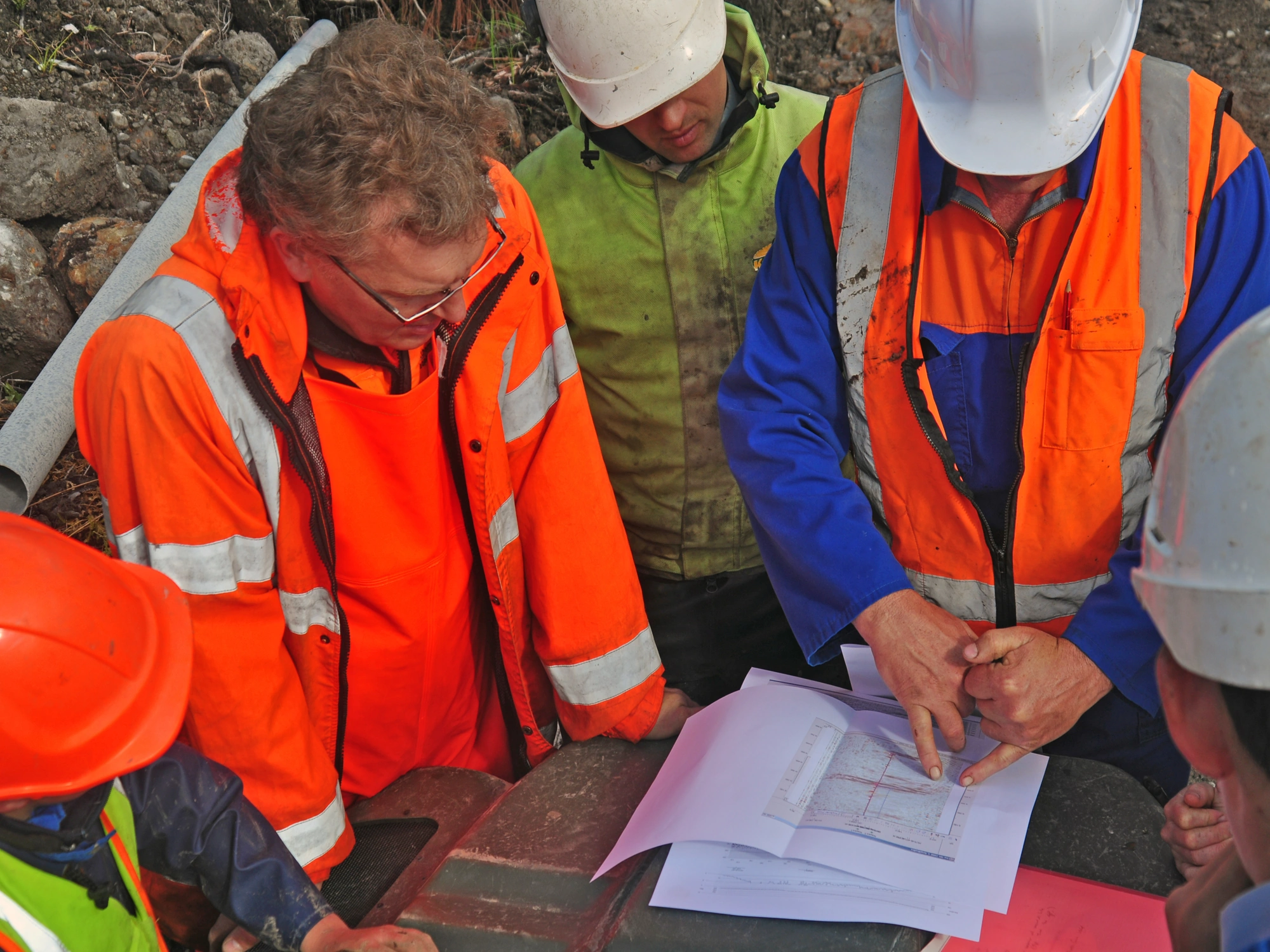Men in hi-vis analysing paper map before collecting land survey data on site.