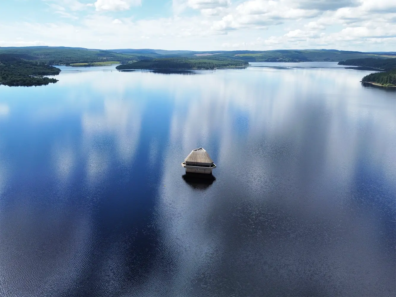 A substantial lake with a small concrete building in the middle of it.