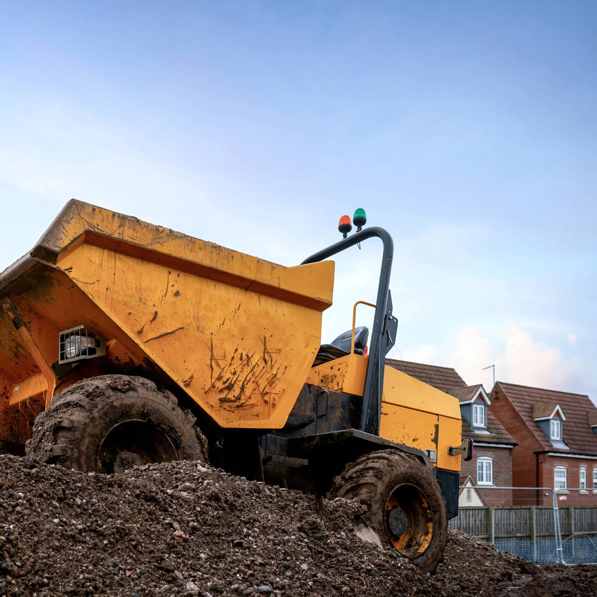 A large yellow vehicle going over a dirt mound on a construction site.