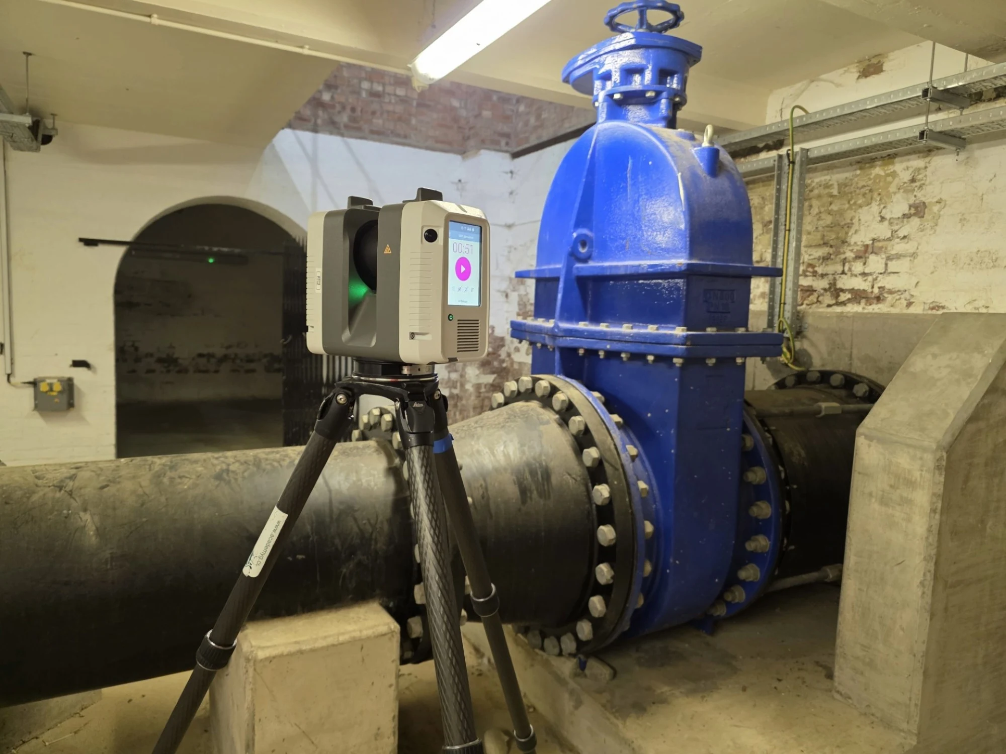 A piece of surveying equipment in front of large pipes.