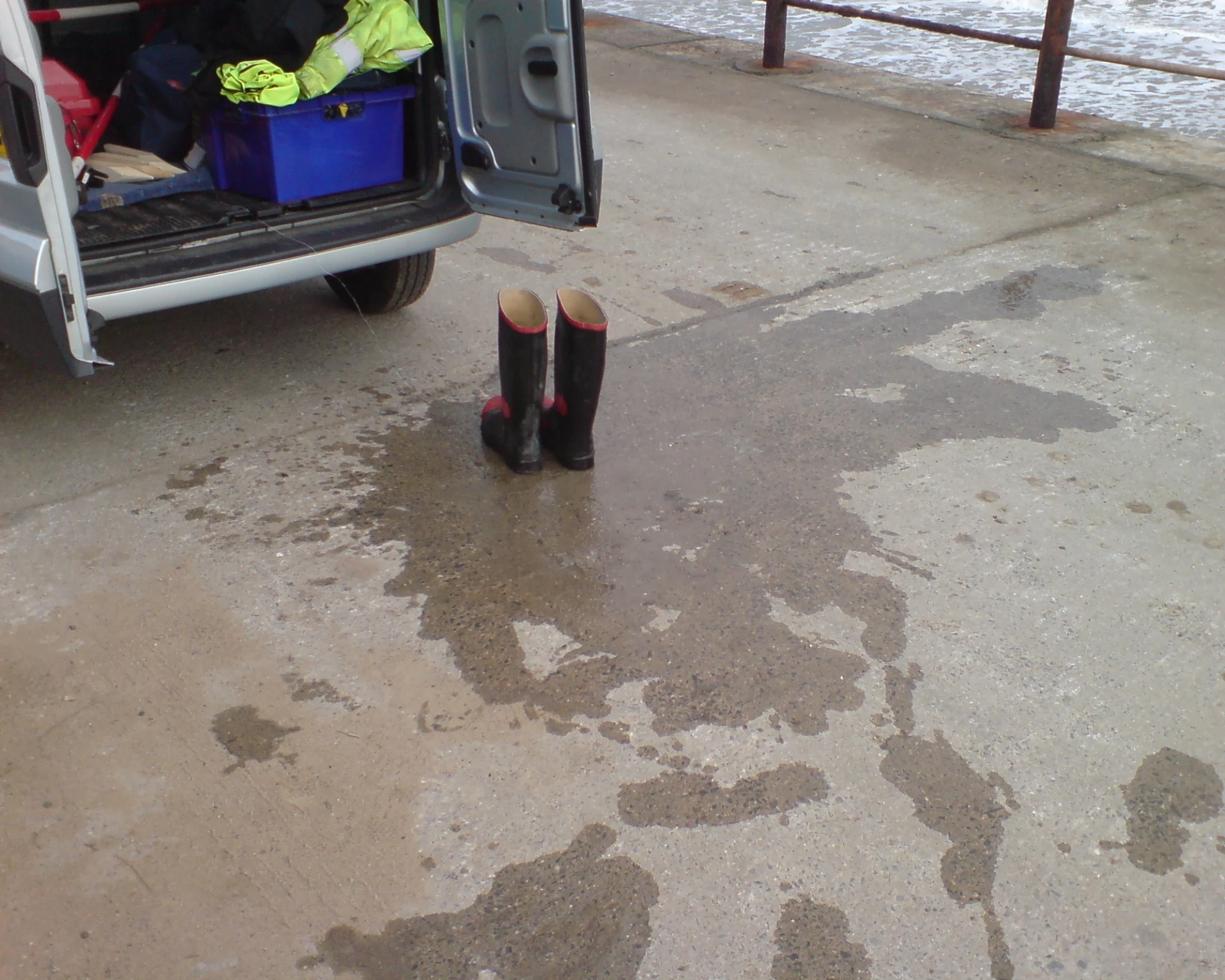 A pair of rubber boots behind a van in a huge wet patch.