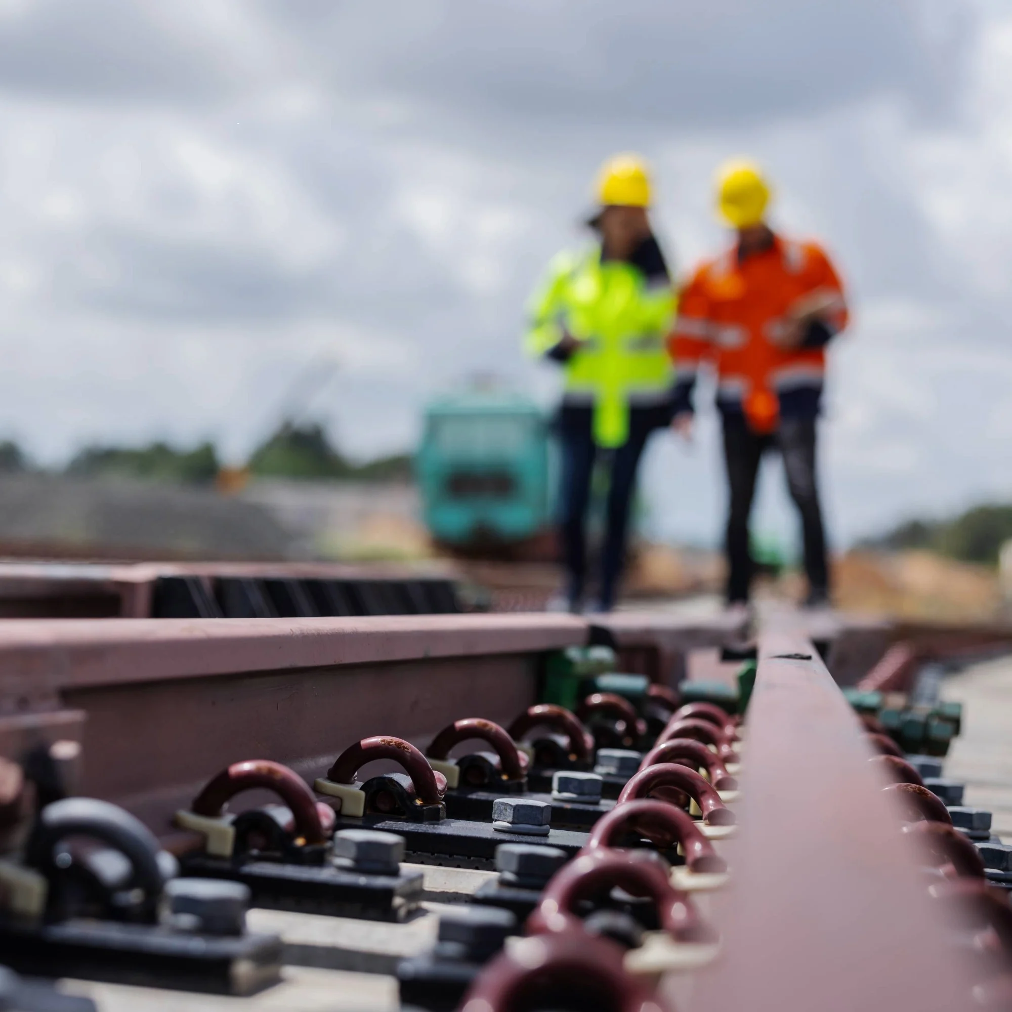 Two people in hi-vis jackets and hardhats walking down a railway.