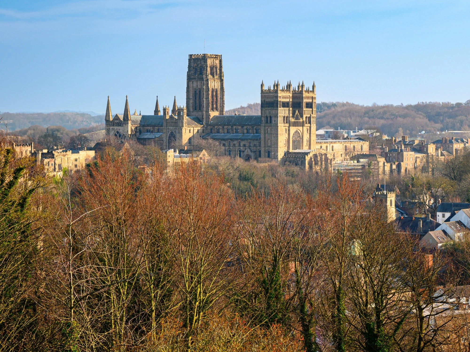Durham Cathedral towering over Durham's town centre in front of a clear, blue sky.