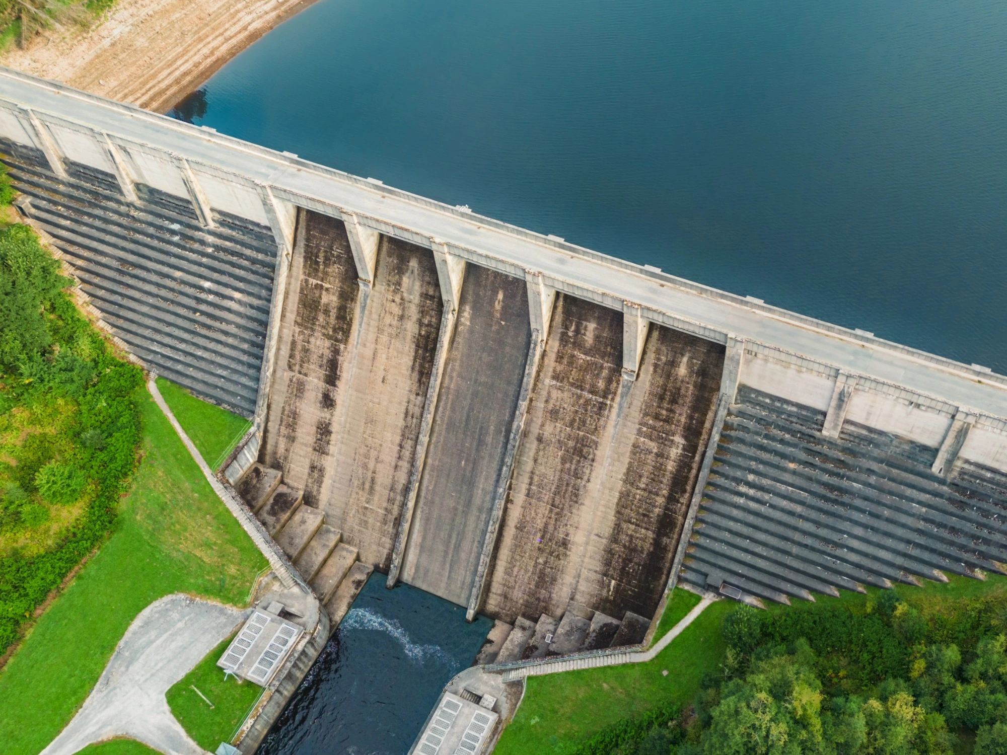 An ariel view of a man-made dam at the edge of a reservoir.