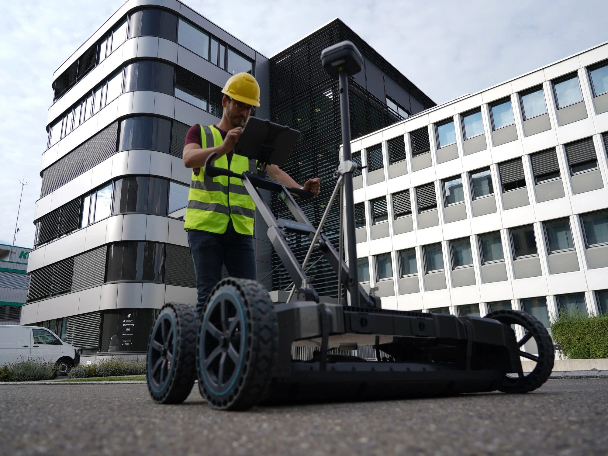 A surveyor pushing GPR survey scanner along a grey concrete path with a tall building in the background.