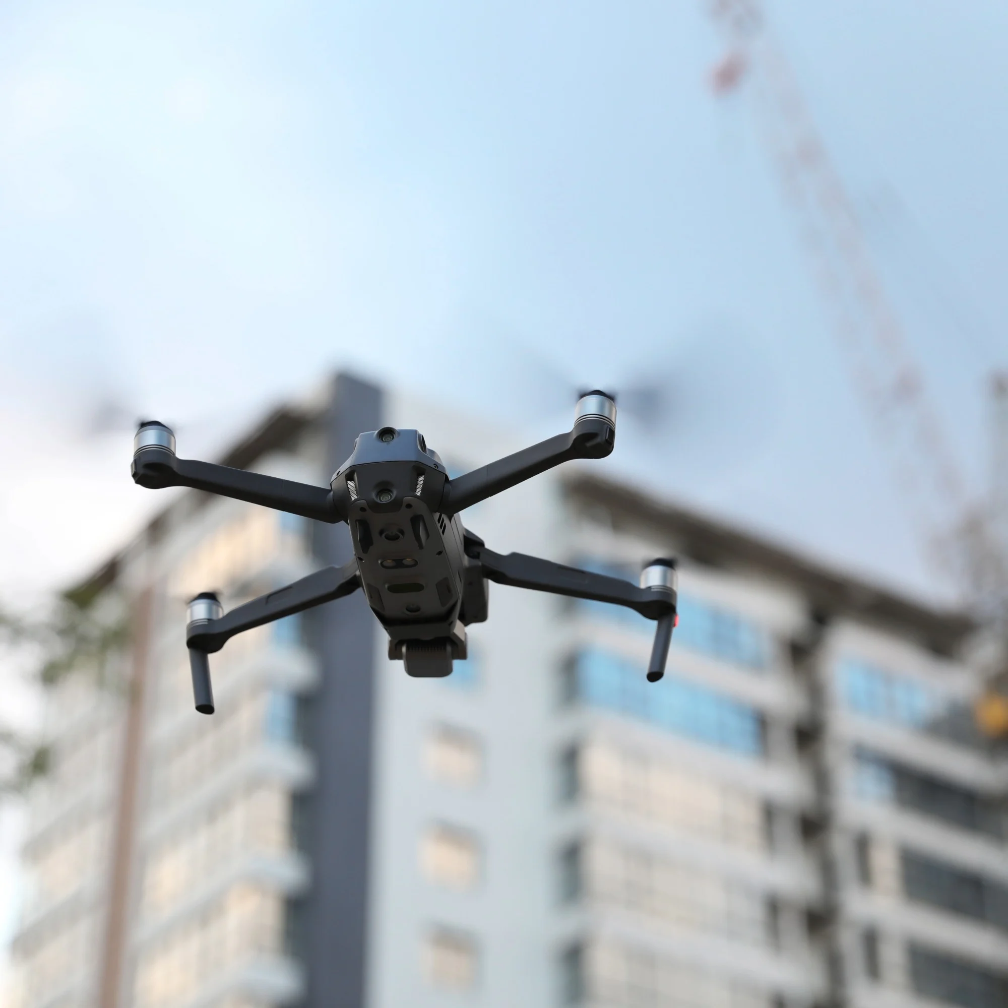 A black drone flying through a large commercial construction site.