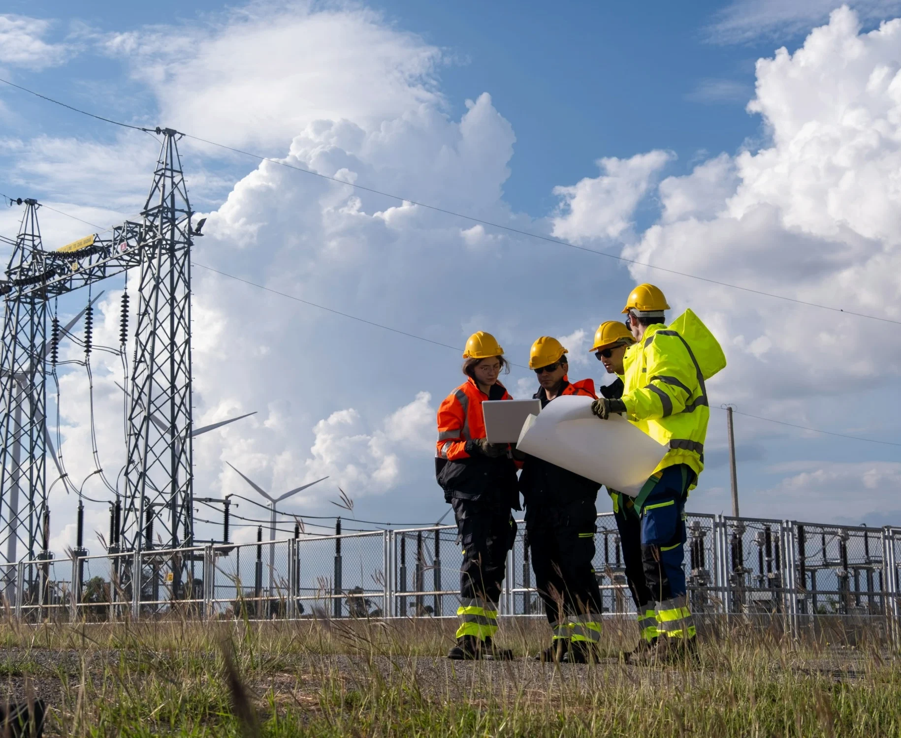 Four surveyors stood in front of an energy plant and cloudy, blue skies, huddled around some paper plans.