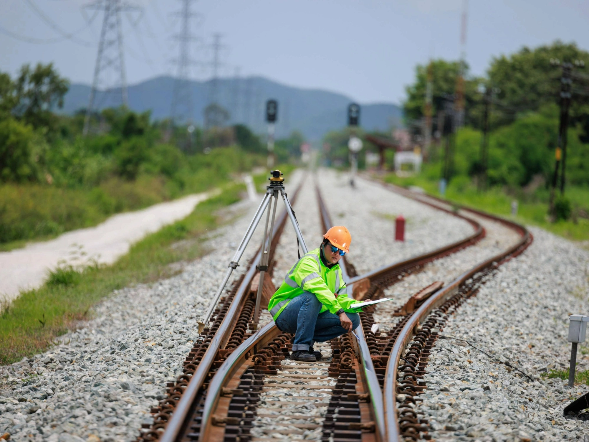 A land surveyor crouched on some rail tracks in from of a total station.