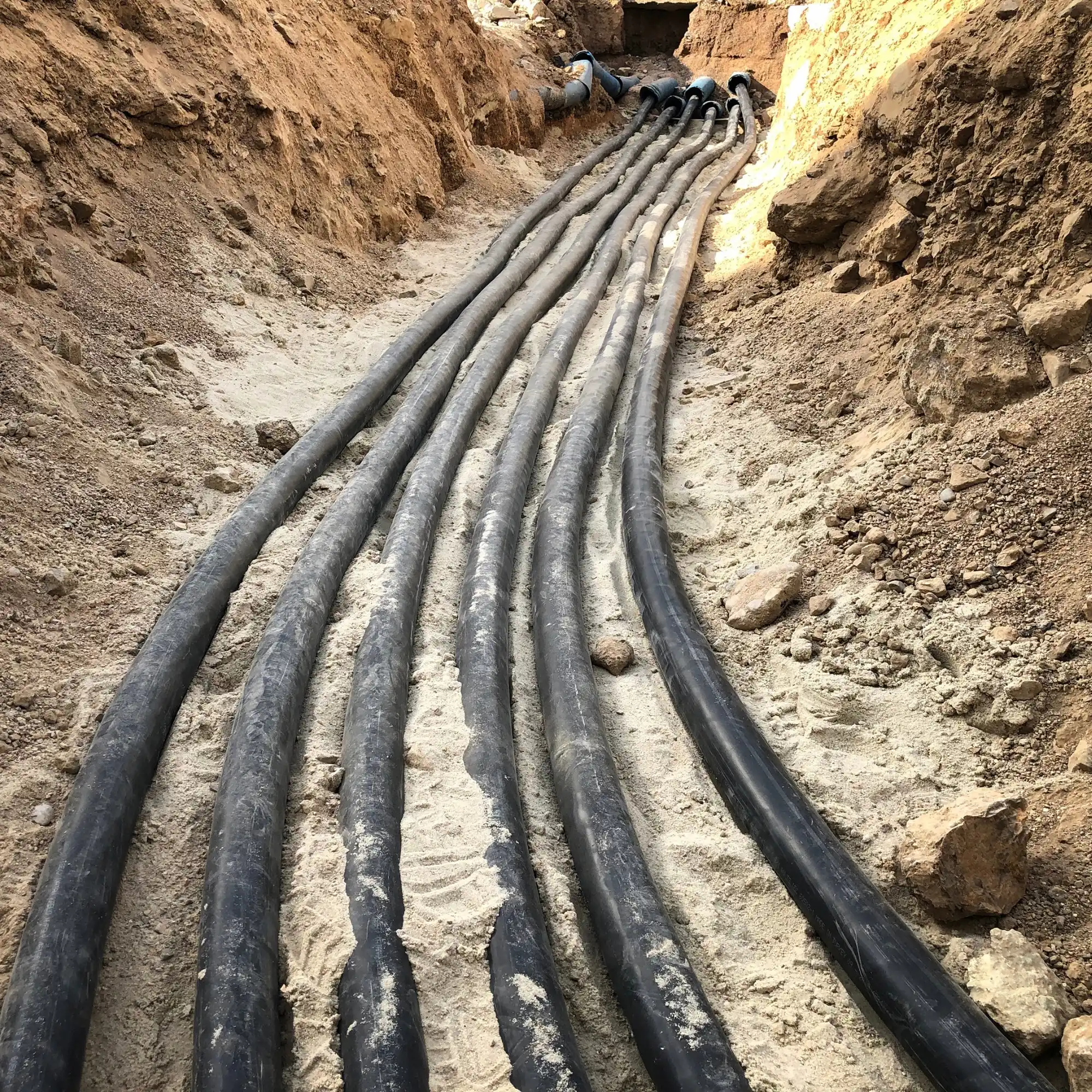 Black cables being laid in a dirt trench.