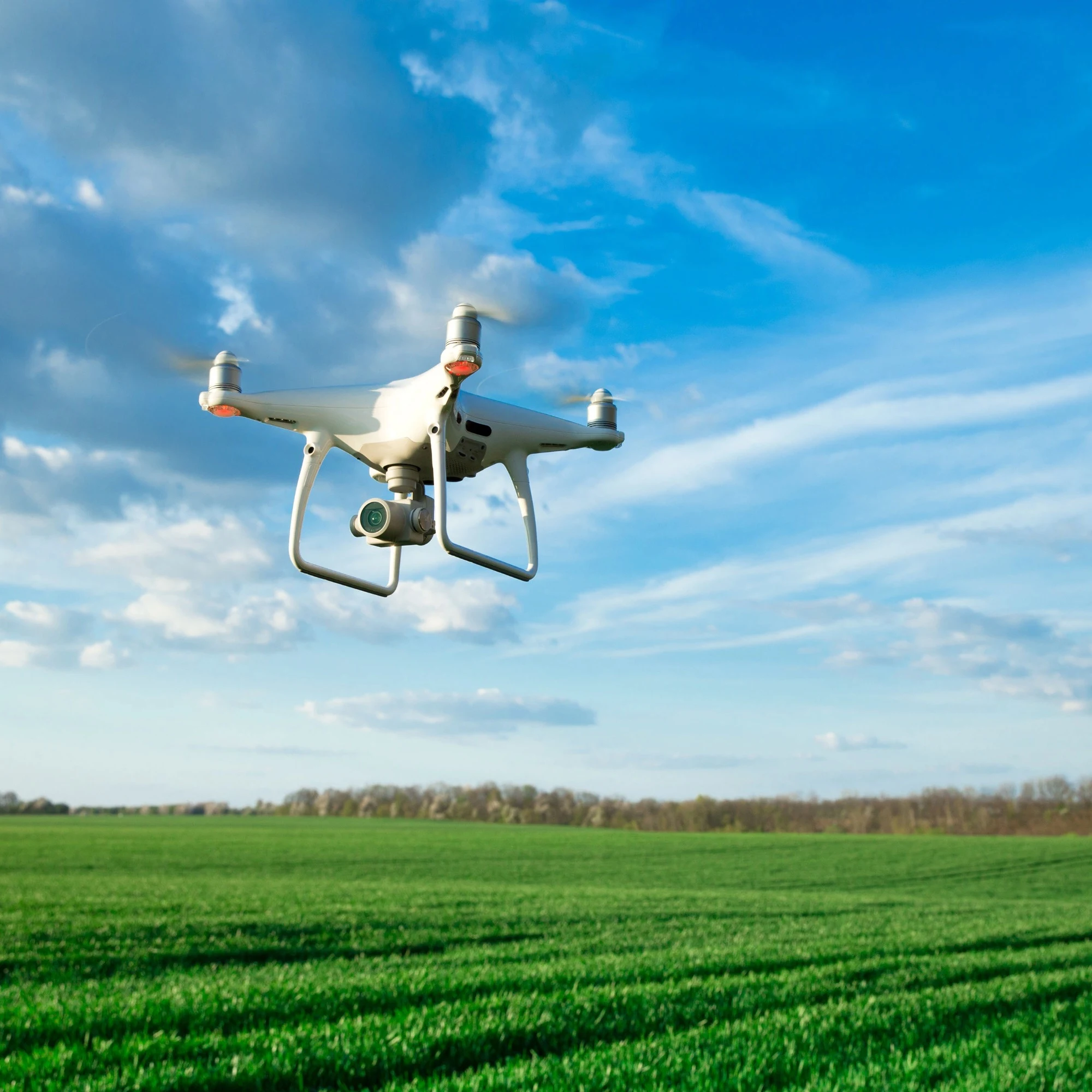 A white drone flying over a crop field.